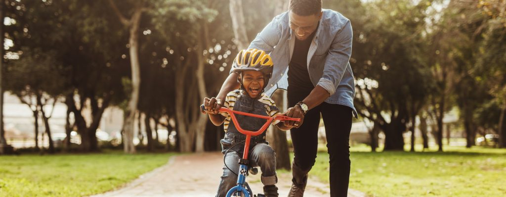 Boy learning to ride a bicycle with his father in park. Father teaching his son cycling at park.